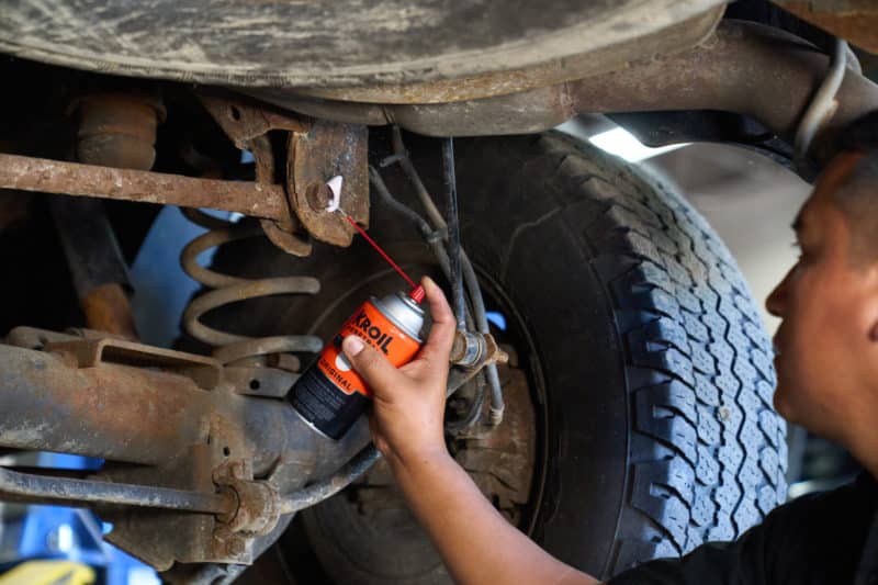 man applying kroil lubricant spray to a rusty truck suspension